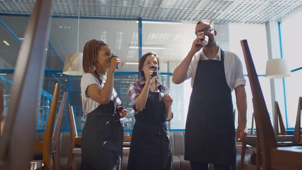 Multiethnic Restaurant Staff in Aprons Toasting with Take-away Coffee Cups Drinking on Closed Cafe