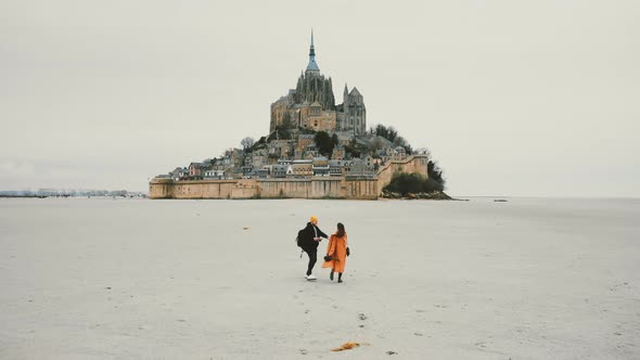 Amazing Cinematic Shot, Drone Follows Happy Couple Hold Hands Walking Towards Epic Mont Saint Michel