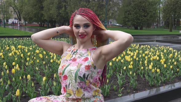 A Girl with Bright Makeup and African Rainbow Braids is Enjoying the Arrival of Spring in Blooming