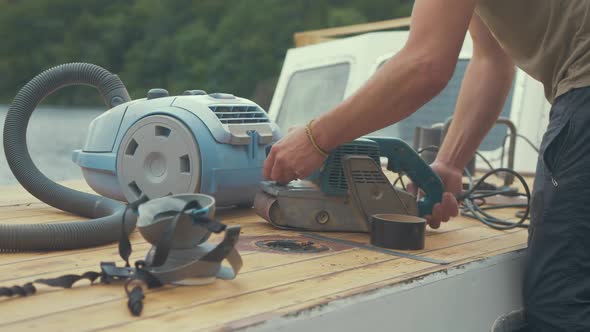 Carpenter setting up belt sander and hoover to sand wood boat roof planks