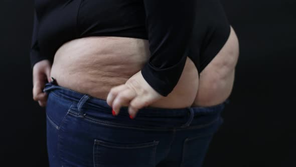 Fat Woman with Cellulite Trying to Put on Jeans on Black Background