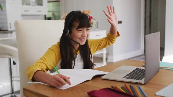 Happy asian girl at home, sitting at desk smiling during online school lesson using laptop