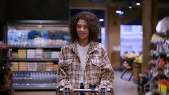 Pretty African American Woman Walks Through Supermarket with Cart