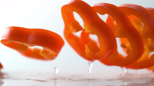 Sliced red pepper falling on water surface. Slow Motion.
