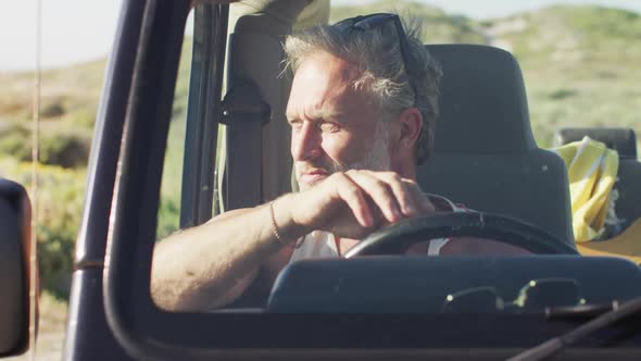 Thoughtful caucasian man sitting in car looking away on sunny day at the beach