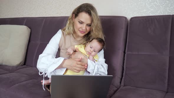 Young Woman with Toddler in Arms Typing on Laptop Concept of Female Freelancers on Maternity Leave