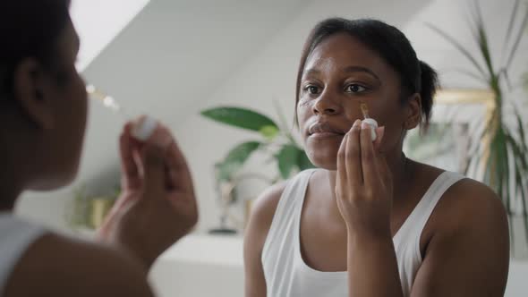 African-American woman using serum to face in the bathroom. Shot with RED helium camera in 4K.