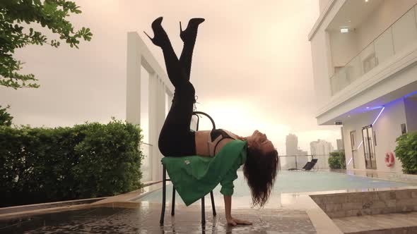 Dancer Posing With Legs In Air On Chair At Poolside