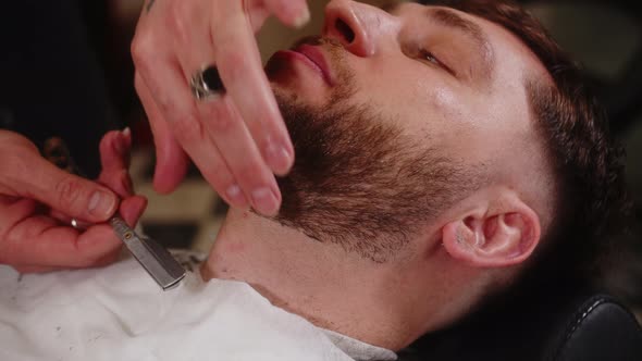 An Adult Man of Arab Appearance Cuts His Beard to a Young Caucasian Guy in a Barbershop