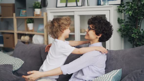 Slow Motion of Loving Mother and Little Son Hugging Sitting on Sofa at Home