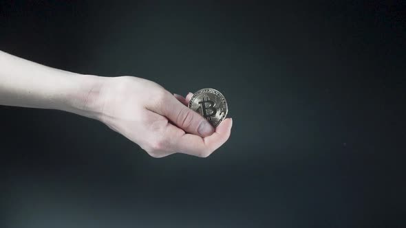 Hand holding Bitcoin coin against black background, slow motion shot.