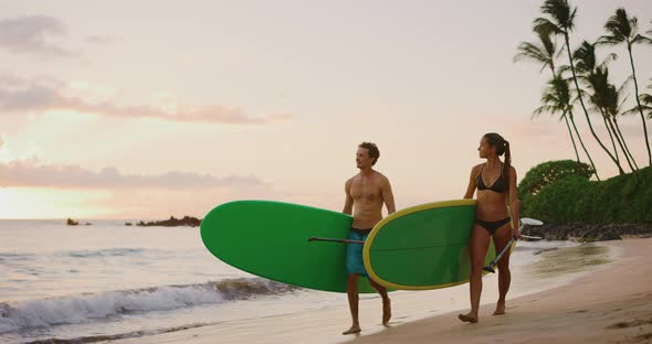 Happy couple walking with stand up paddle boards on the beach
