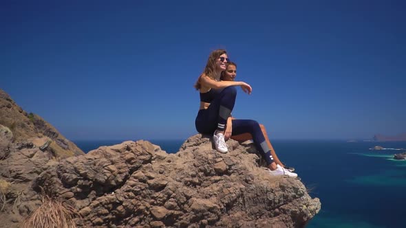 Aerial View of Two Happy Girls Sitting on Hilltop and Admiring the Landscape of Tropical Islands