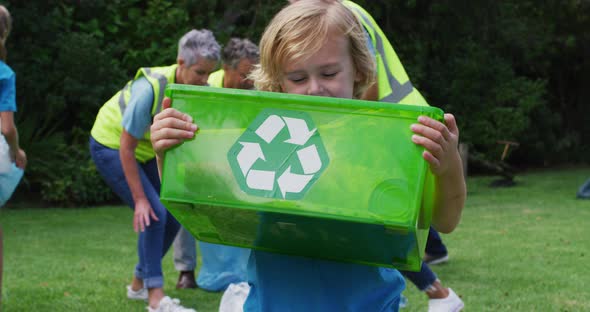 Smiling caucasian boy holding recycling box picking up litter with volunteers in field