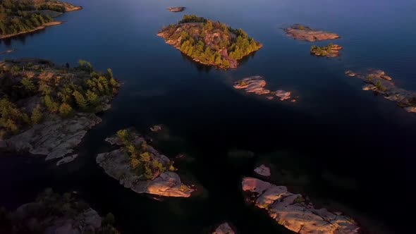 Rocky Granite Islands with Green Pine Trees in Blue Lake at Sunset, Drone Aerial Wide Tilt Reveal. F