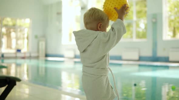 Cute Little Boy Throwing a Yellow Ball to the Pool at the Leisure Center