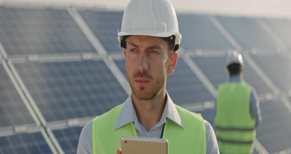 Close Up View of Male Engineer Looking at Tablet Screen and Than Aside. Man in Hard Helmet and