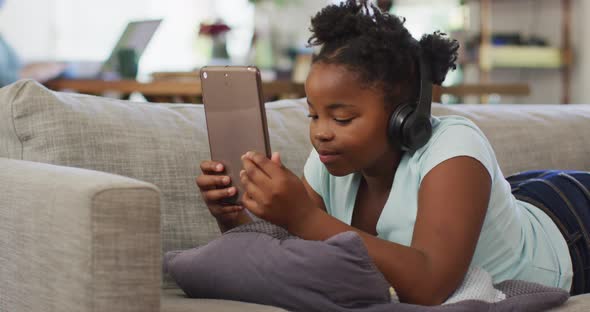 Happy african american girl lying on sofa using tablet