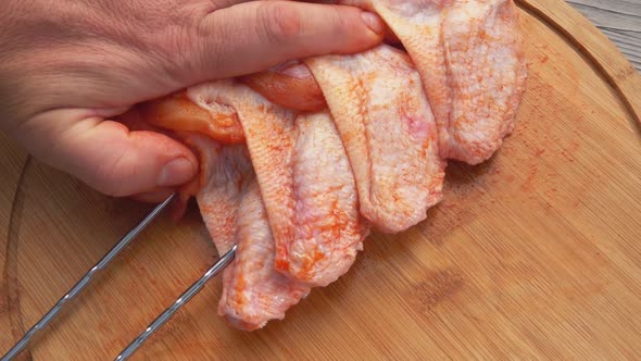 Male Hands Are Piercing the Raw Chicken Wings with Skewers on the Wooden Board