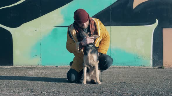 A Beggar is Petting His Dog Next to the Graffiti Wall