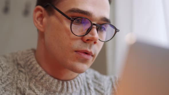 Concentrated man wearing eyeglasses working by laptop