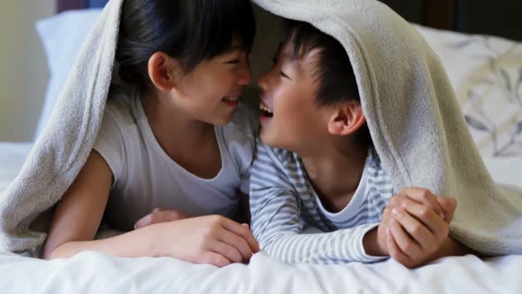 Siblings relaxing under blanket in bedroom 4k