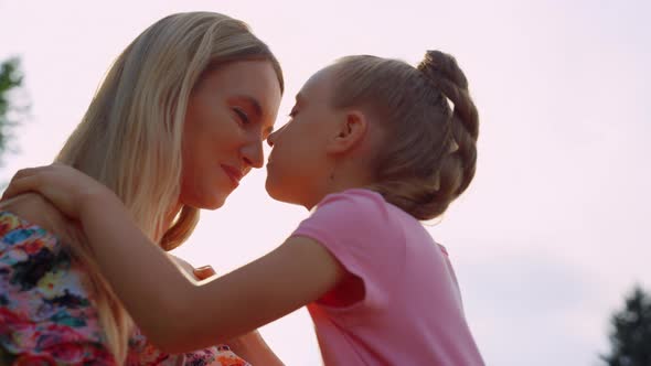 Cute Mother and Daughter Looking at Each Other in City Park in Sunset