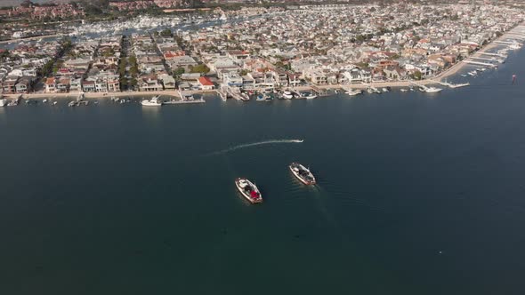 Aerial shot orbiting around two ferries crossing paths in Newport Harbor with anchored boats and bui