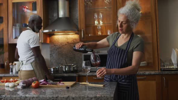 Caucasian senior woman wearing apron pouring wine in the glass in the kitchen at home