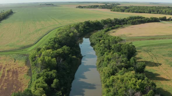 Aerial, still river stream running through agricultural grass farm land fields