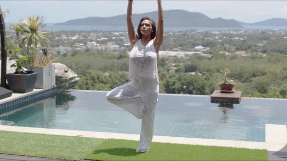 Calm Woman Practicing Yoga Poolside Against Beautiful Landscape of Sea Shore