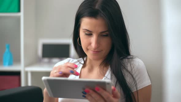 Brunette Women Using a Tablet Pc Sitting on the Sofa in a Living Room