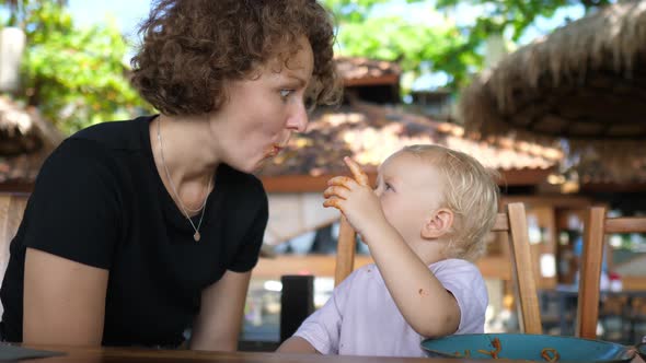 Caucasian Baby Feed Her Young Mother Tomato Pasta with Hands