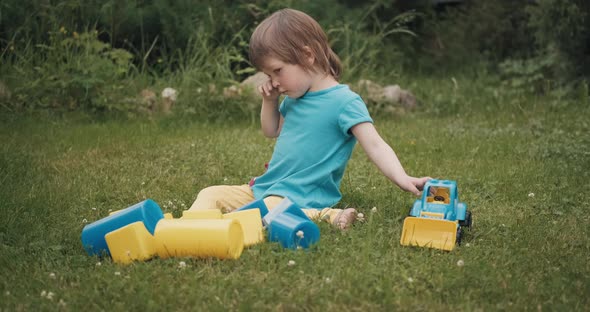 Small Caucasian Child is Sitting on the Grass and Crying Loudly