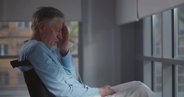 Side View of Sick Aged Man with Nasal Oxygen Tube in Wheelchair Feeling Unwell