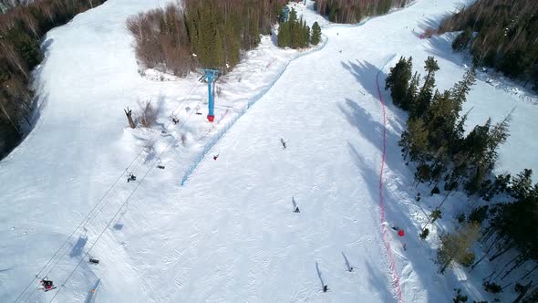 Aerial Top Down View on a Ski Slope Surrounded with Trees People Snowboarding and Skiing Down the