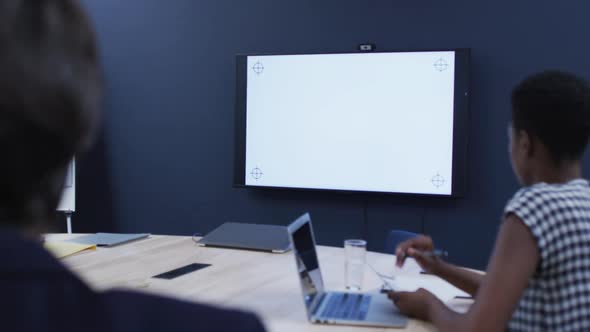 Diverse business colleagues sitting looking at screen in office meeting