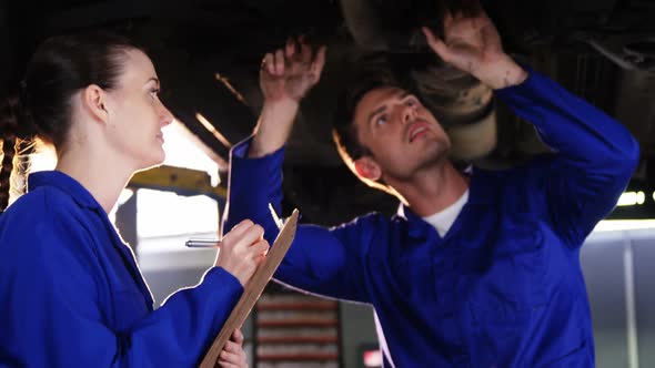 Female mechanic writing on clipboard while male mechanic checking a car