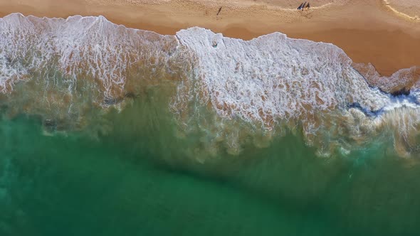 Aerial View of Waves Surf on a Sandy Beach Where Tourists Walk on the Sand During Their Vacation