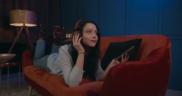 A Young Girl Listens To Music Lying on the Couch and Waving Her Legs To the Rhythm of the Music