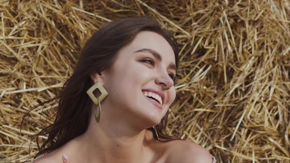 Girl with Blowing Hair Gently Caressing Her Neck and Looking Into Camera at Hay