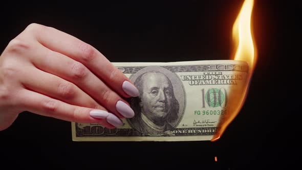 Woman Holding Burning American Hundred Dollar Banknote on Black Background