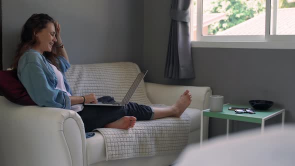 A Young Woman with a Laptop Sitting on the Couch and Makes a Video Call