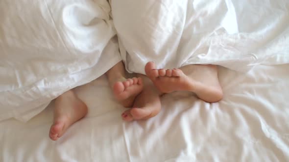 Closeup of Mom's Feet and a Small Child Under a White Blanket on the Bed