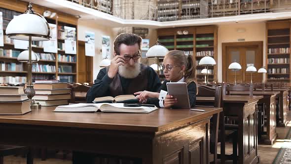 Senior Bearded Grandpa with Glasses Reading His 10-aged Granddaughter Interesting Book