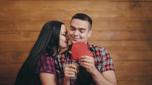 Long-haired woman flirting with her boyfriend and he is carving out of paper red heart