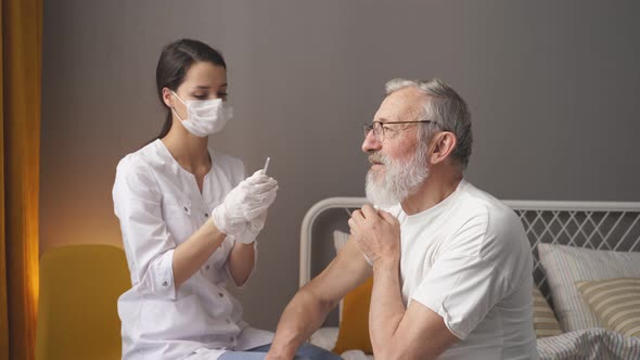 Nurse in White Coat Making an Injection in Hand to Senior Patient at Home