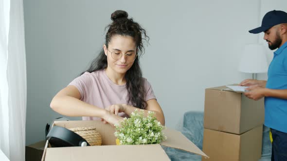 Young Woman Unpacking Things Then Signing Papers and Talking to Freight Mover in New House