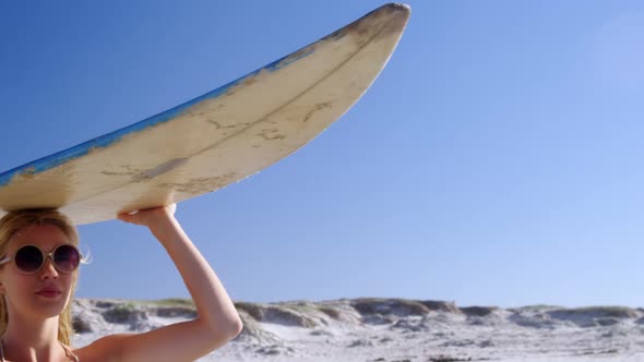 Young woman carrying surfboard on head at beach