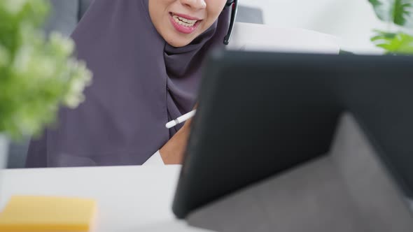 Asia muslim lady wear headphone using tablet talk to colleagues about sale report in video call.